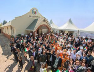 Crowd in front of worship building waving mini INC/South African flags