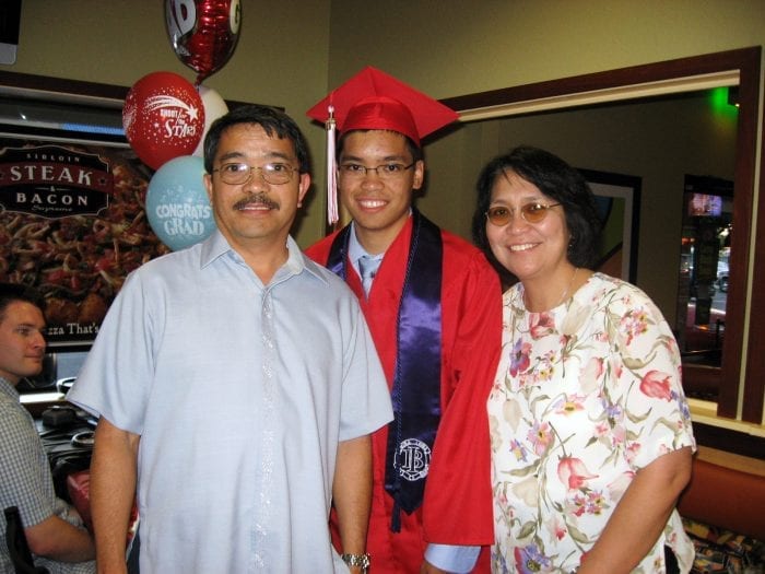 male student in cap and gown with parents