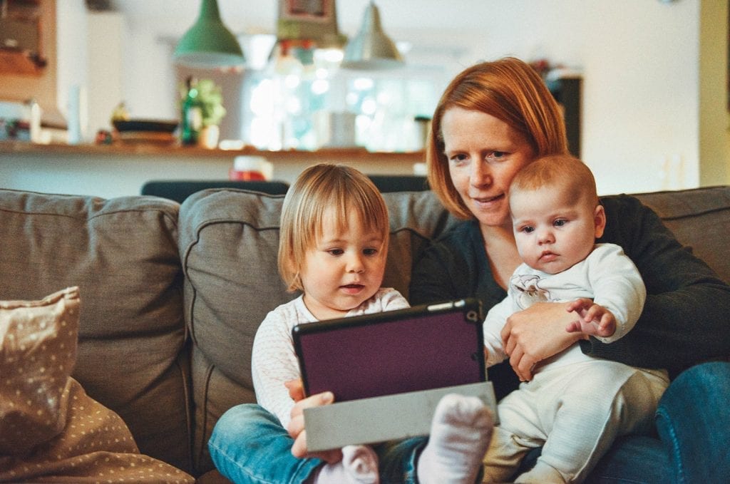 Mom with two kids watching a tablet while sitting
on a couch.