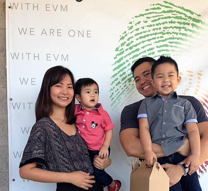 A family of 4 posing in front of a “We Are One with EVM” poster.