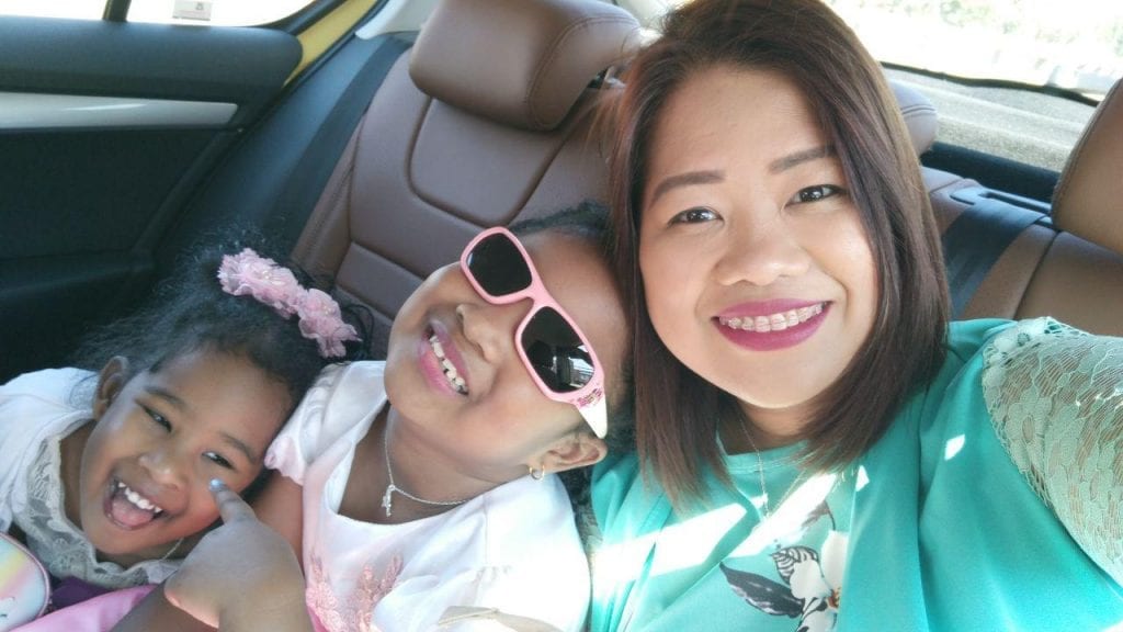 A mom and two daughters in a car smiling.