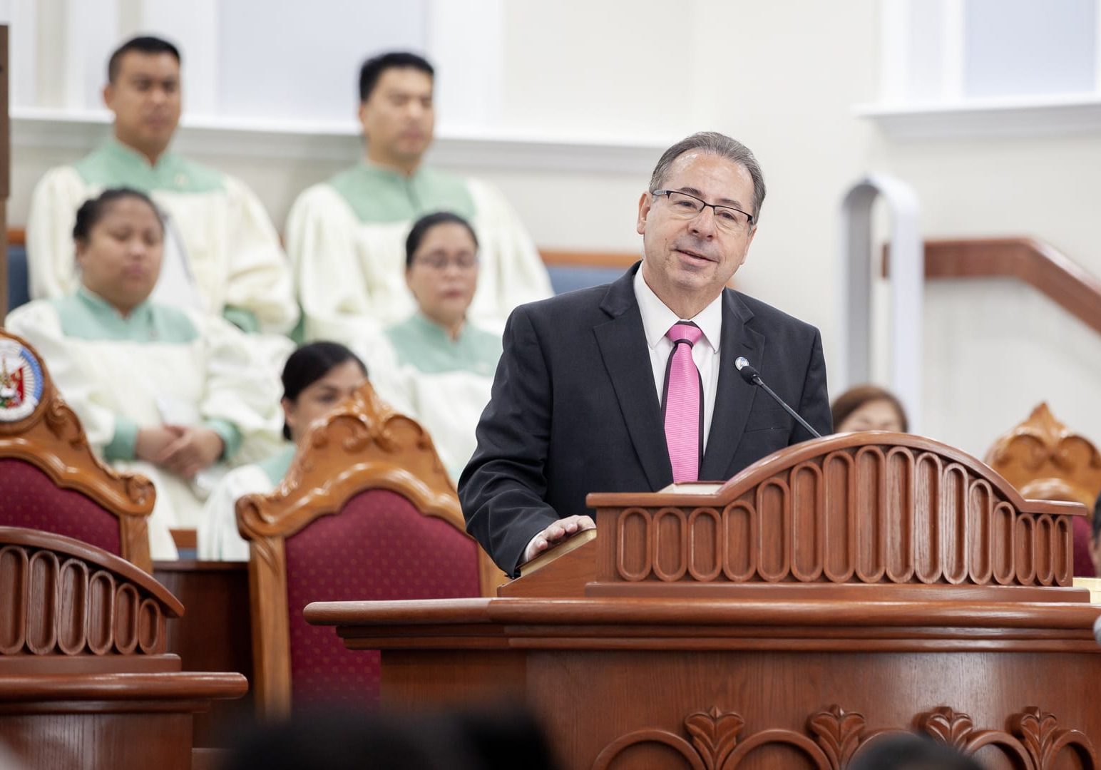 minister preaching at podium with choir members in the background