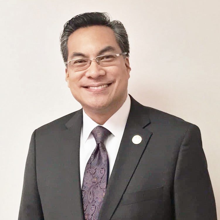 minister smiling, wearing a suit, purple tie, and glasses